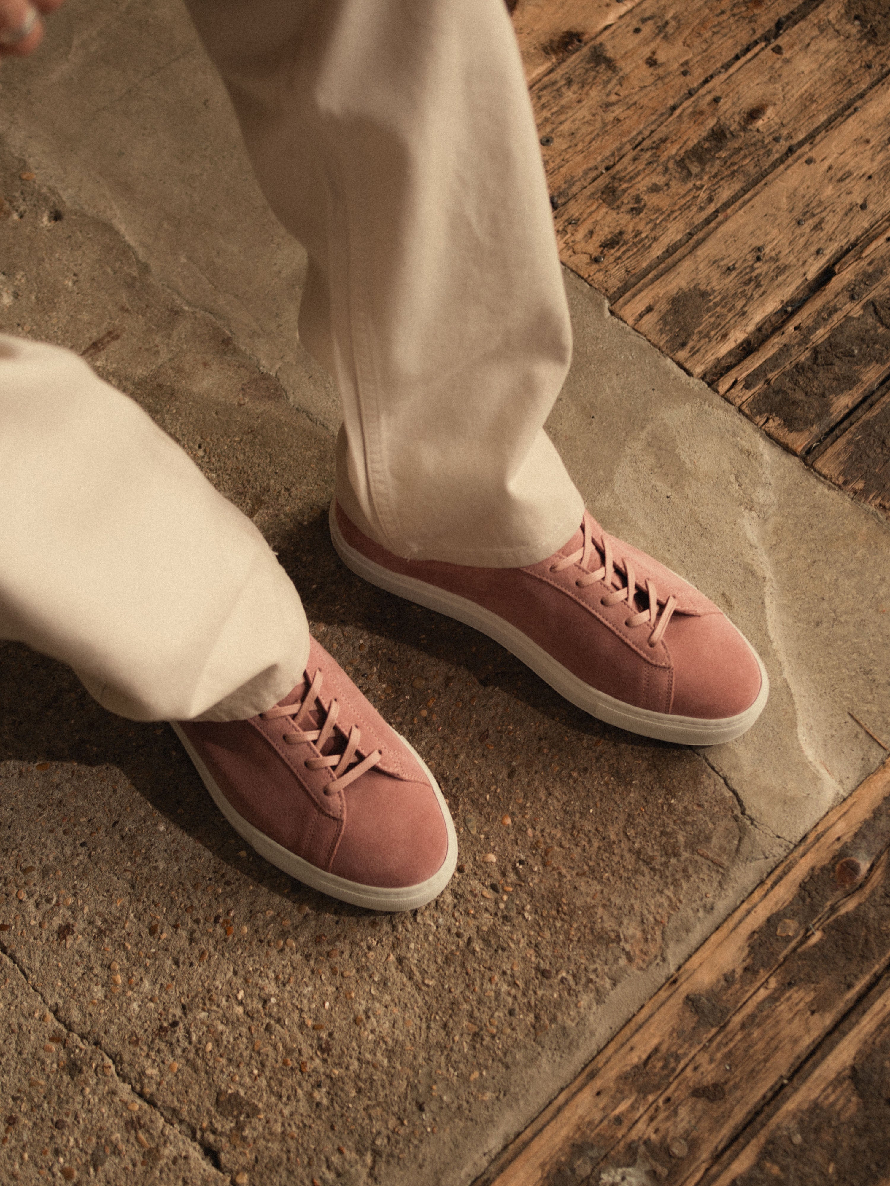 Legs of a person wearing deep blush suede sneakers with matching laces and white rubber soles and beige chino pants